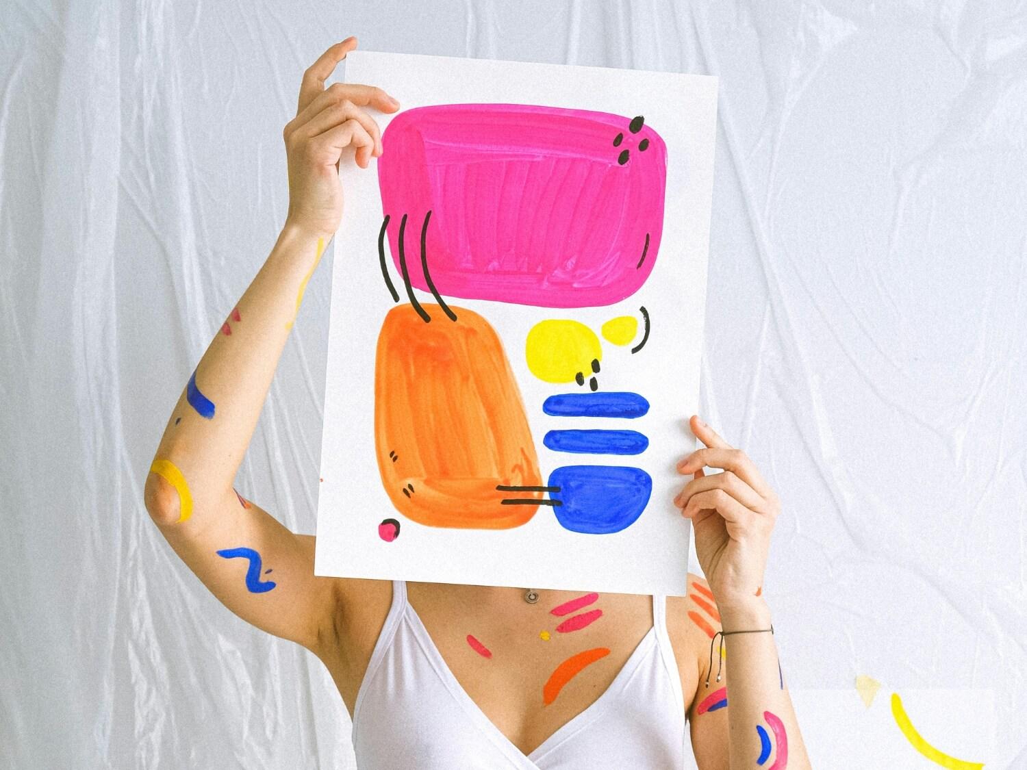 Photo of a woman holding a painting with paint on her body.