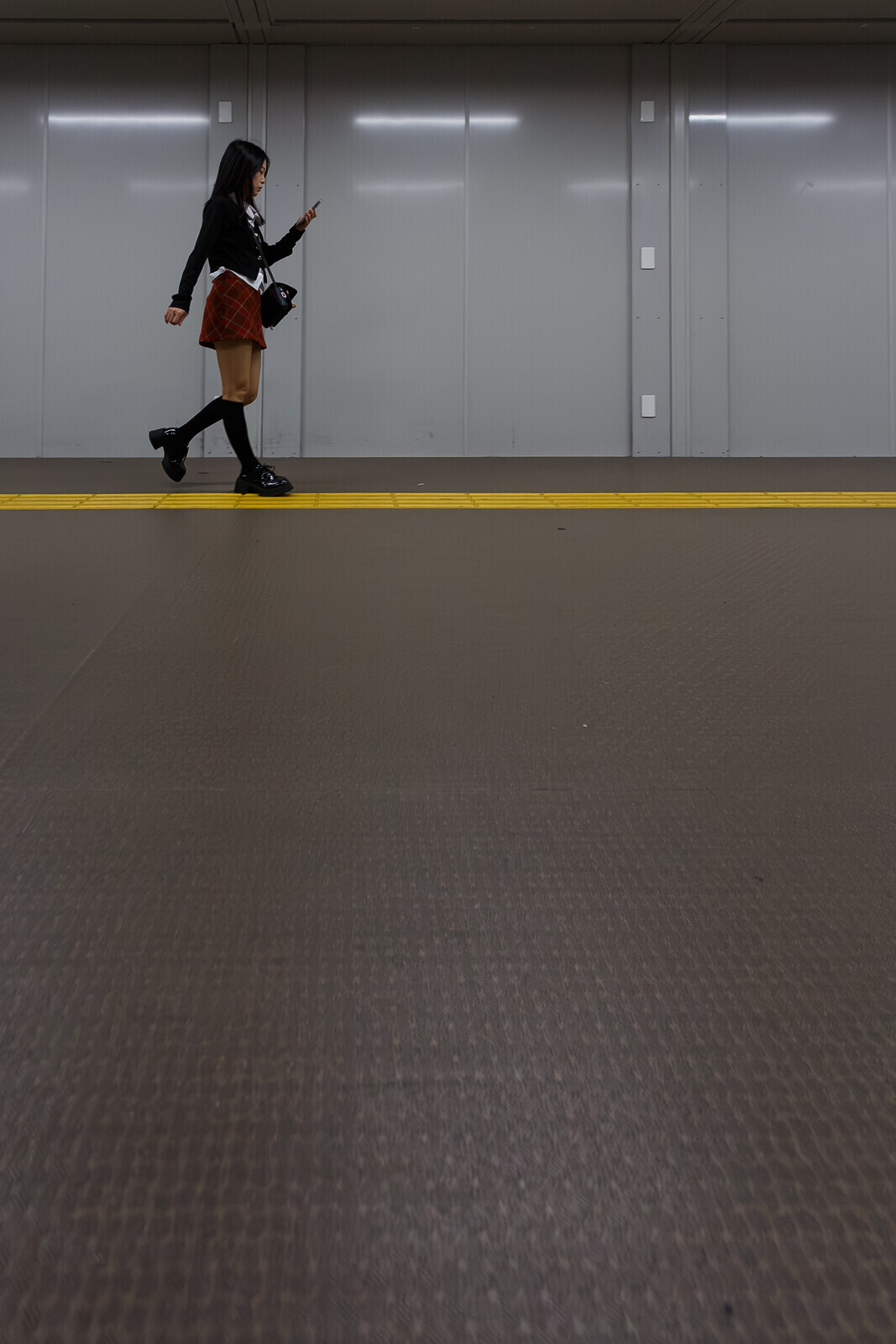 A young Japanese woman walks through Shinjuku Station while using her smartphone. Shinjuku, Tokyo, Japan. Saturday, October 18th, 2025