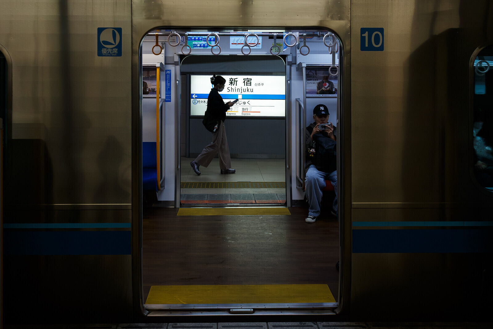 A woman using a smart phone walks past a Shinjuku sign on the Odakyu line platform of Shinjuku station, Shinjuku, Tokyo, Japan. Saturday, October 25th, 2025