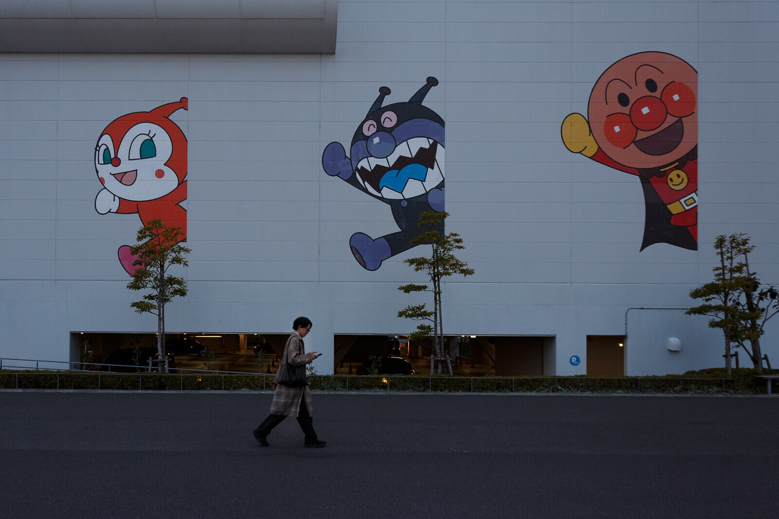 A man, using a smart phone, walks past the  Yokohama Anpanman Children's Museum with large character images of (Right to Left) Anpanman, Baikinman and Dokin-chan on the wall. Yokohama, Kanagawa, Japan. Saturday, march 14th, 2026