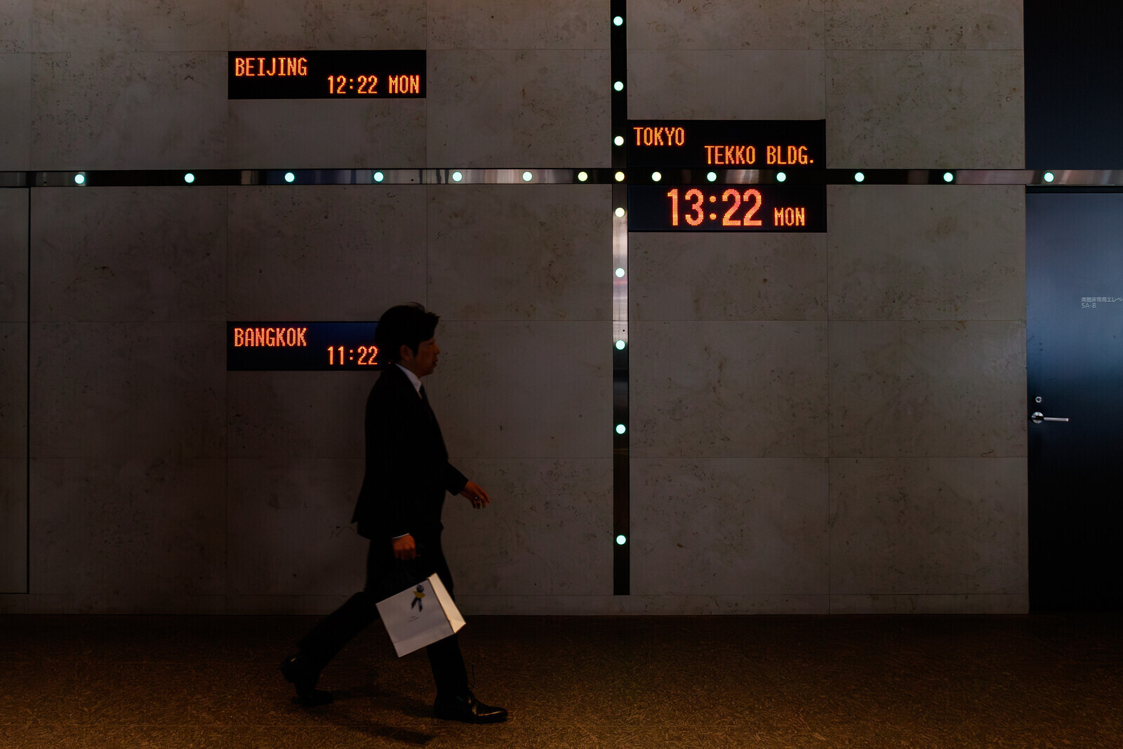 A Japanese salaryman or male office worker walks past a wall showing the time in Tokyo, Bangkok and Beijing in the Tekko Building, Marunouchi, Tokyo, Japan. Monday, March 30th, 2026 The Tekko building is a n office and transport facility near Tokyo station.